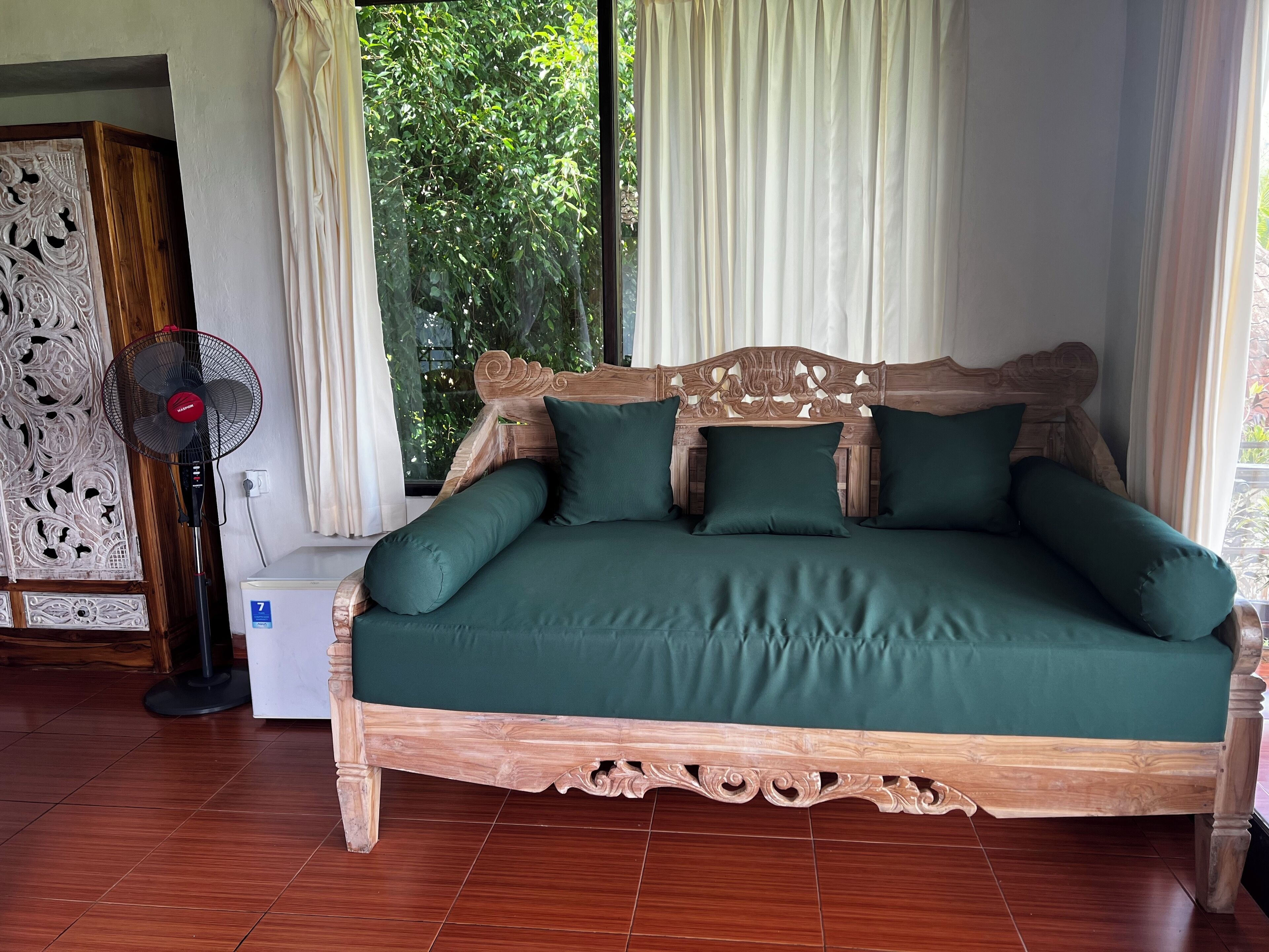 Un letto di legno con biancheria verde, una ventola da terra e un pannello decorativo a parete.