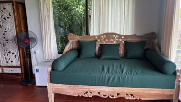 Un letto di legno con biancheria verde, una ventola da terra e un pannello decorativo a parete.