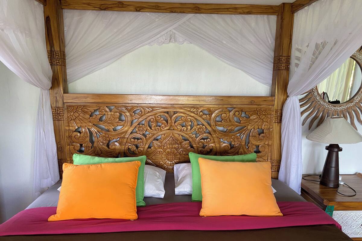 A bed with a wooden headboard, two orange pillows, one green pillow, and a pink bedspread.