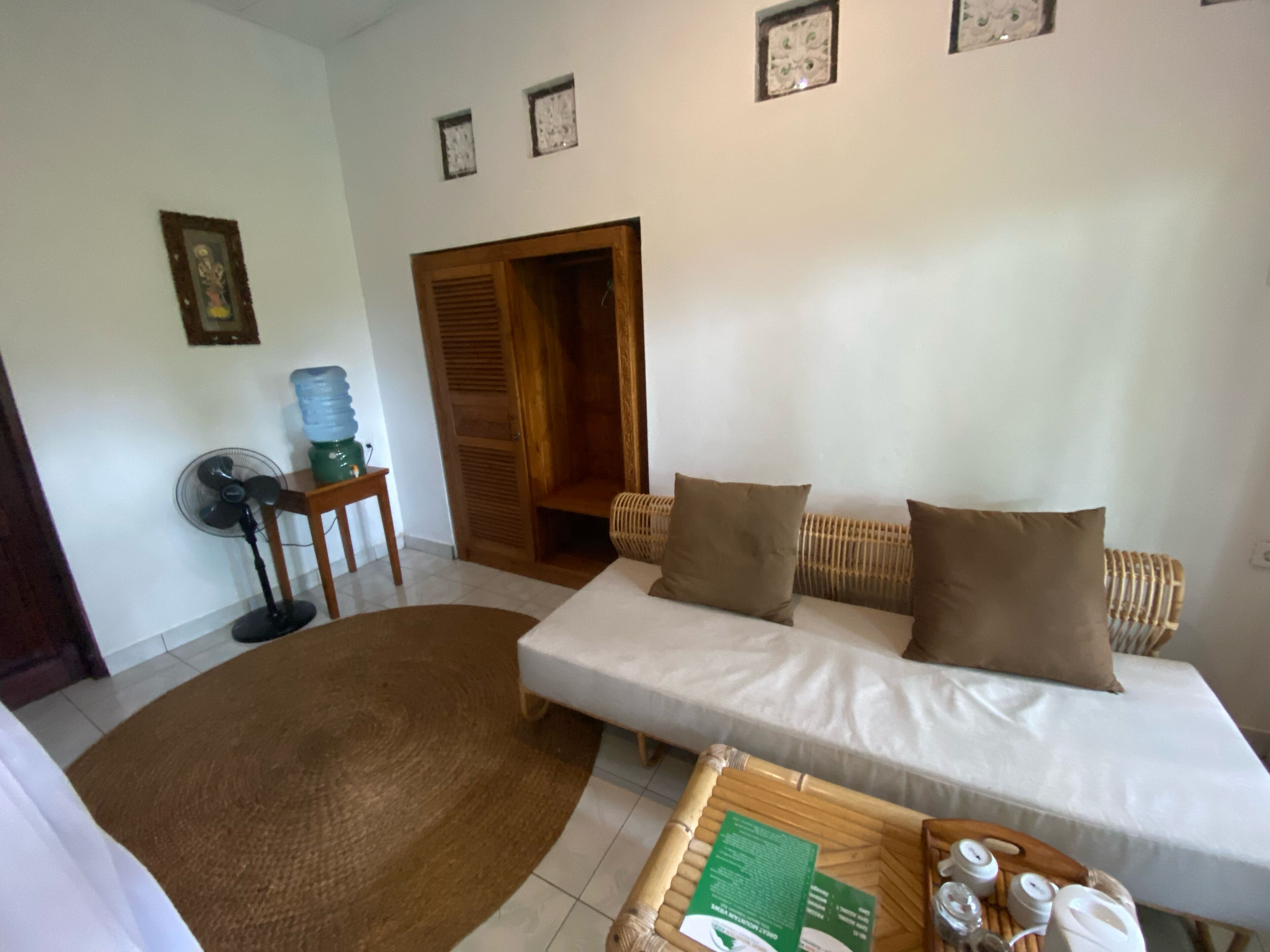 Una sala de estar con un sofá, un ventilador, un dispensador de agua y una puerta.