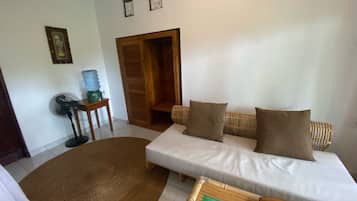 Una sala de estar con un sofá, un ventilador, un dispensador de agua y una puerta.