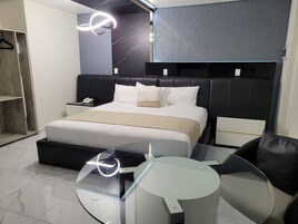 Una habitación de hotel moderna con una cama, mesitas de noche, una mesa de centro de vidrio y una zona de estar.