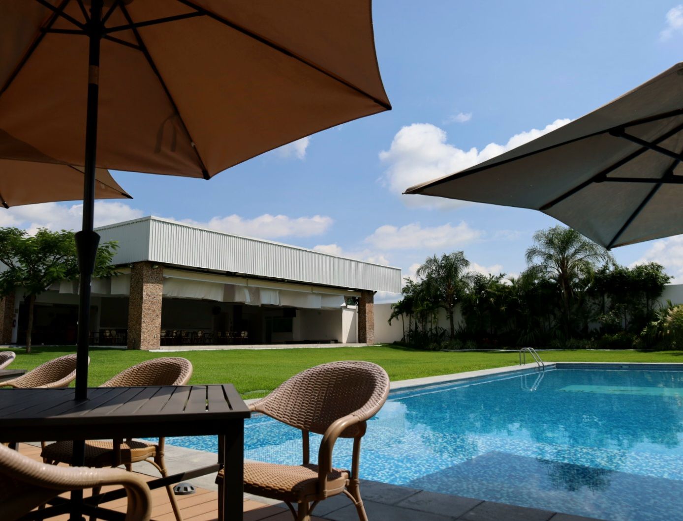 Zona junto a la piscina con asientos al aire libre, un porche cubierto y vista de un edificio al fondo.
