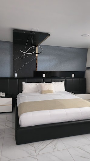 Un dormitorio moderno con cabecera negra, cama con ropa blanca y piso con estampado de mármol.