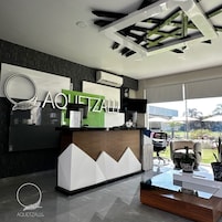 Un mostrador de recepción moderno con un logotipo, un televisor de pantalla plana y una zona de estar con vistas al exterior.