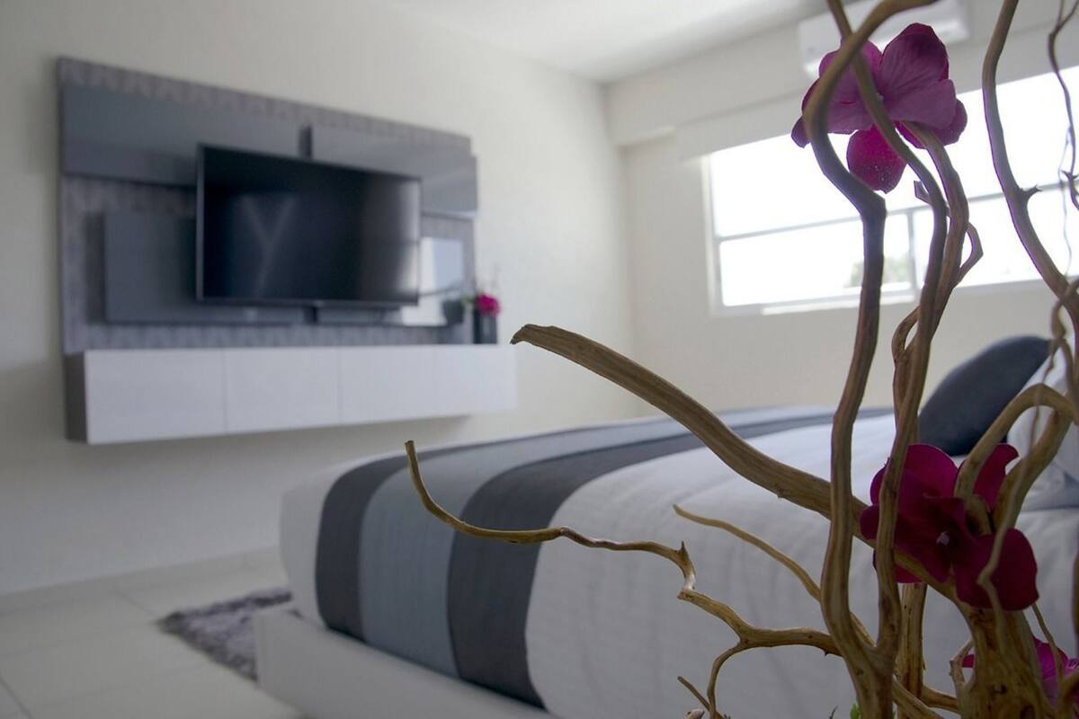 A modern bedroom with a bed, a mounted TV, and a window.