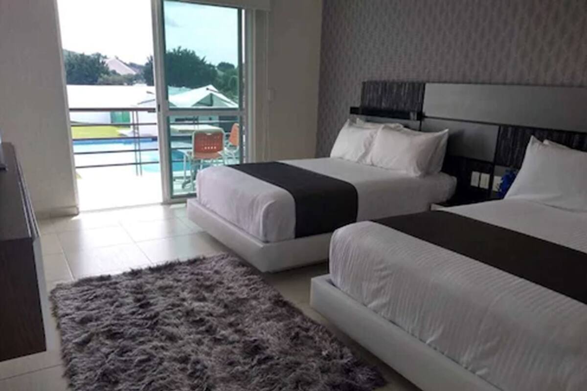 A hotel room with two beds, a large window, and a view of a pool and greenery outside.