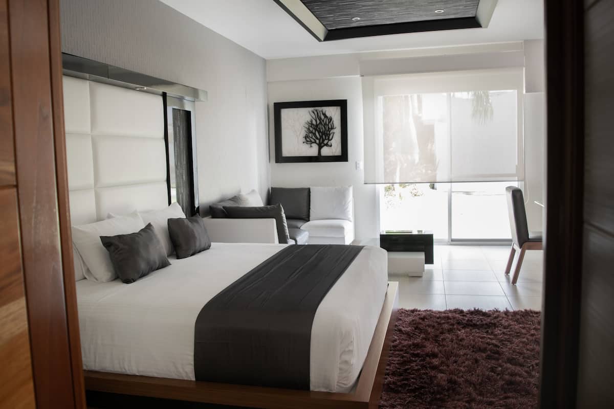 A modern bedroom with a large bed, a nightstand, a chair, and a framed artwork on the wall.