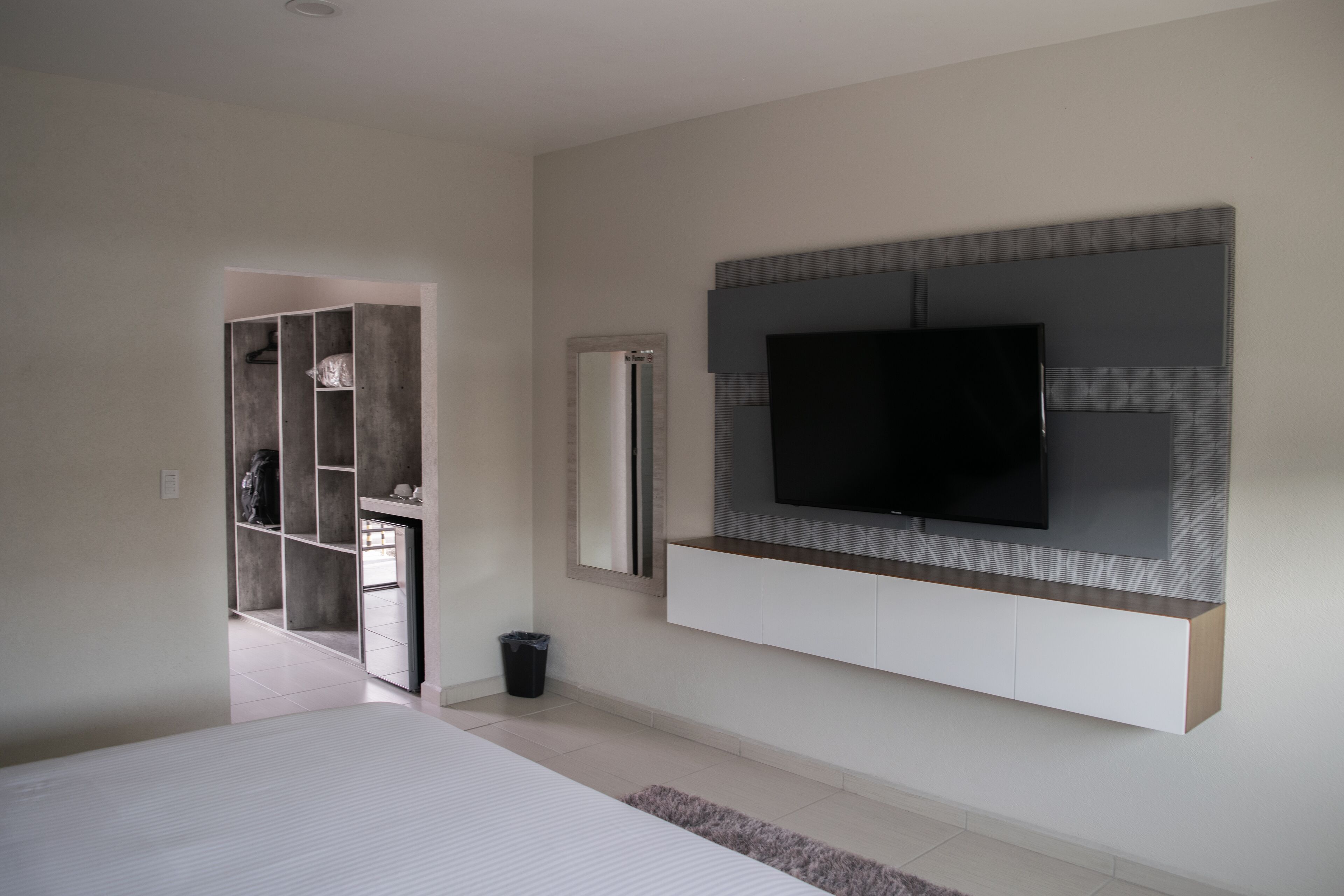 A modern bedroom with a large bed, a TV mounted on the wall, and a walk-in closet.