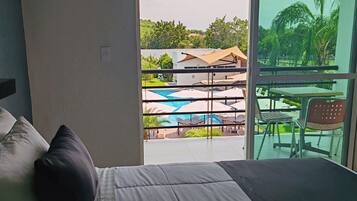 Habitación de hotel con cama, vista a una piscina y zona de estar exterior.