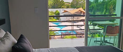A hotel room with a bed, a view of a pool and outdoor seating area.