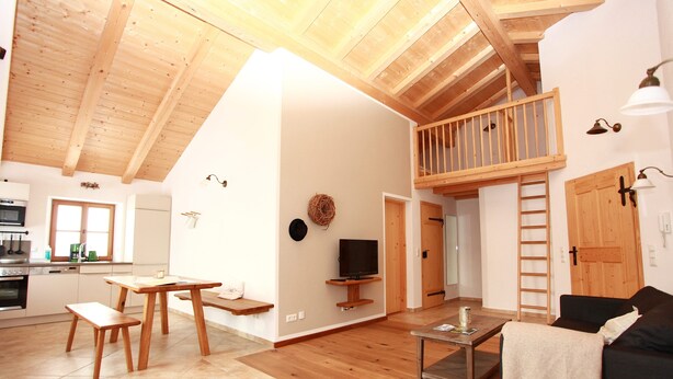 A spacious living area with wooden floors, a loft bedroom with a wooden railing, a dining area with a table and benches, and a kitchen with modern appliances. - Vacation apartment Amelie, 70 sqm, balcony, 2 bedrooms (Schechen)