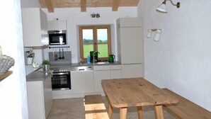 A compact kitchen with a wooden table and bench, a window with a view of a green field, and a wall-mounted light fixture. - Vacation apartment Amelie, 70 sqm, balcony, 2 bedrooms (Schechen)