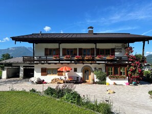 A two-story building with a balcony, outdoor seating, and a dog. - FeWo Jenner, 1-2 Personen, 60 qm (Schönau am Königssee)