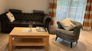 Een woonkamer met een donkergrijze bank, een houten salontafel en een grijze fauteuil.