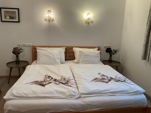 A neatly made bed with white linens and a floral design, two bedside tables with lamps, and a wall-mounted light fixture.