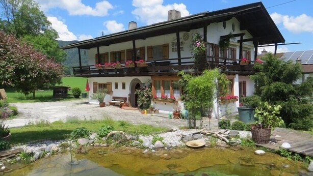 Een klassiek chalet met een balkon, een kleine tuin en een vijver.