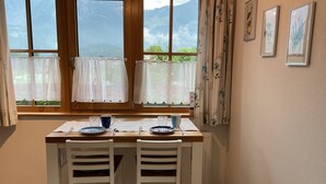 Een eetgedeelte met een houten tafel, twee witte stoelen en een raam met gordijnen.
