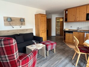 Ein modernes Wohnzimmer mit einer Couch, zwei karierten Sesseln, einem kleinen Tisch und einer Küchenzeile mit Holzschränken und einer Mikrowelle.