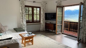 Een gezellige woonkamer met een bank, een klein houten tafeltje, een televisie en uitzicht op bergen door een schuifdeur.