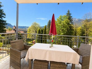 Una terraza con mobiliario de mimbre, una mesa con mantel blanco y una sombrilla roja.