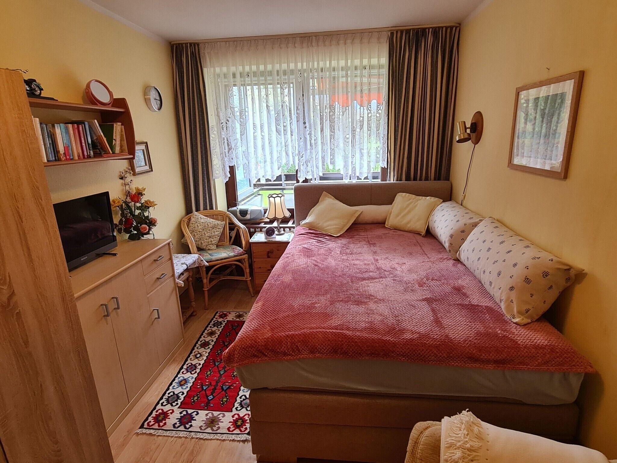 Une chambre confortable avec un lit, un bureau, une chaise, une bibliothèque et un téléviseur.