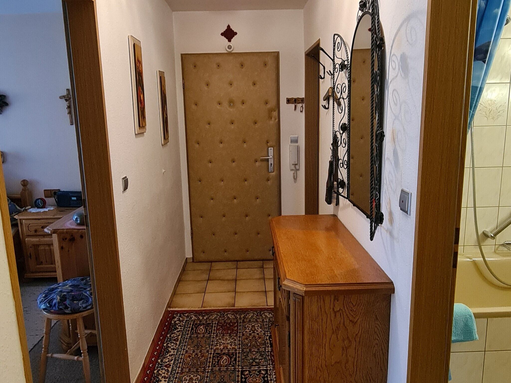 A hallway with a wooden door, a small wooden cabinet, a patterned rug, and a wall-mounted mirror.
