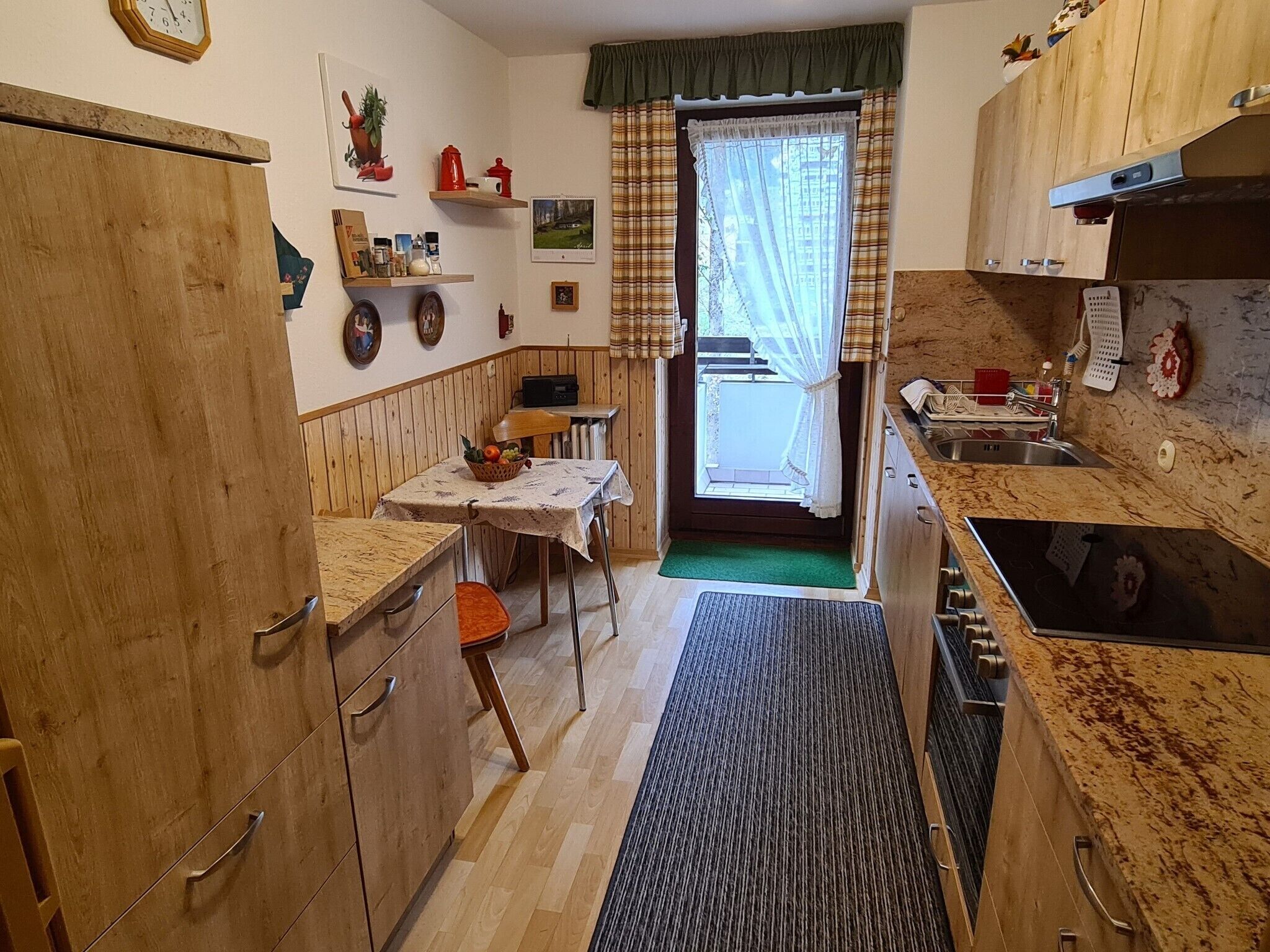 Une cuisine de taille réduite, dotée de meubles en bois, d’une table à manger et d’une petite fenêtre agrémentée de rideaux.