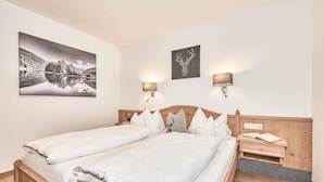 A double bed with white linens, a wooden headboard, two bedside tables with lamps, and a framed deer head artwork on the wall. - (8) Zwei-Raum-Ferienwohnung 38qm, Bad/WC, Extra-Schlafraum, Küche, Balkon (Reit im Winkl)