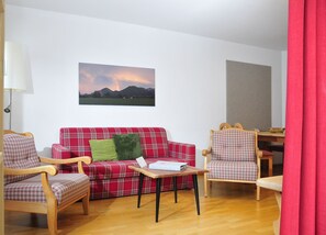 Sala de estar com sofá xadrez vermelho, duas cadeiras de madeira, uma mesinha e um abajur.