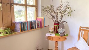 A cozy reading nook with a wooden bookshelf, a small round table with a plant, and a chair. - Ferienwohnung Auerberg, bis 4 Personen, 1 seperates Schlafzimmer, Erdgeschoß, Südterrasse (Bad Feilnbach)