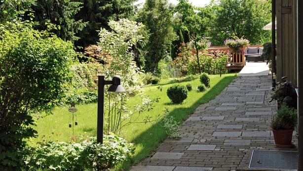 A stone pathway leading to a wooden building with a garden area on one side. - Ferienwohnung Auerberg, bis 4 Personen, 1 seperates Schlafzimmer, Erdgeschoß, Südterrasse (Bad Feilnbach)