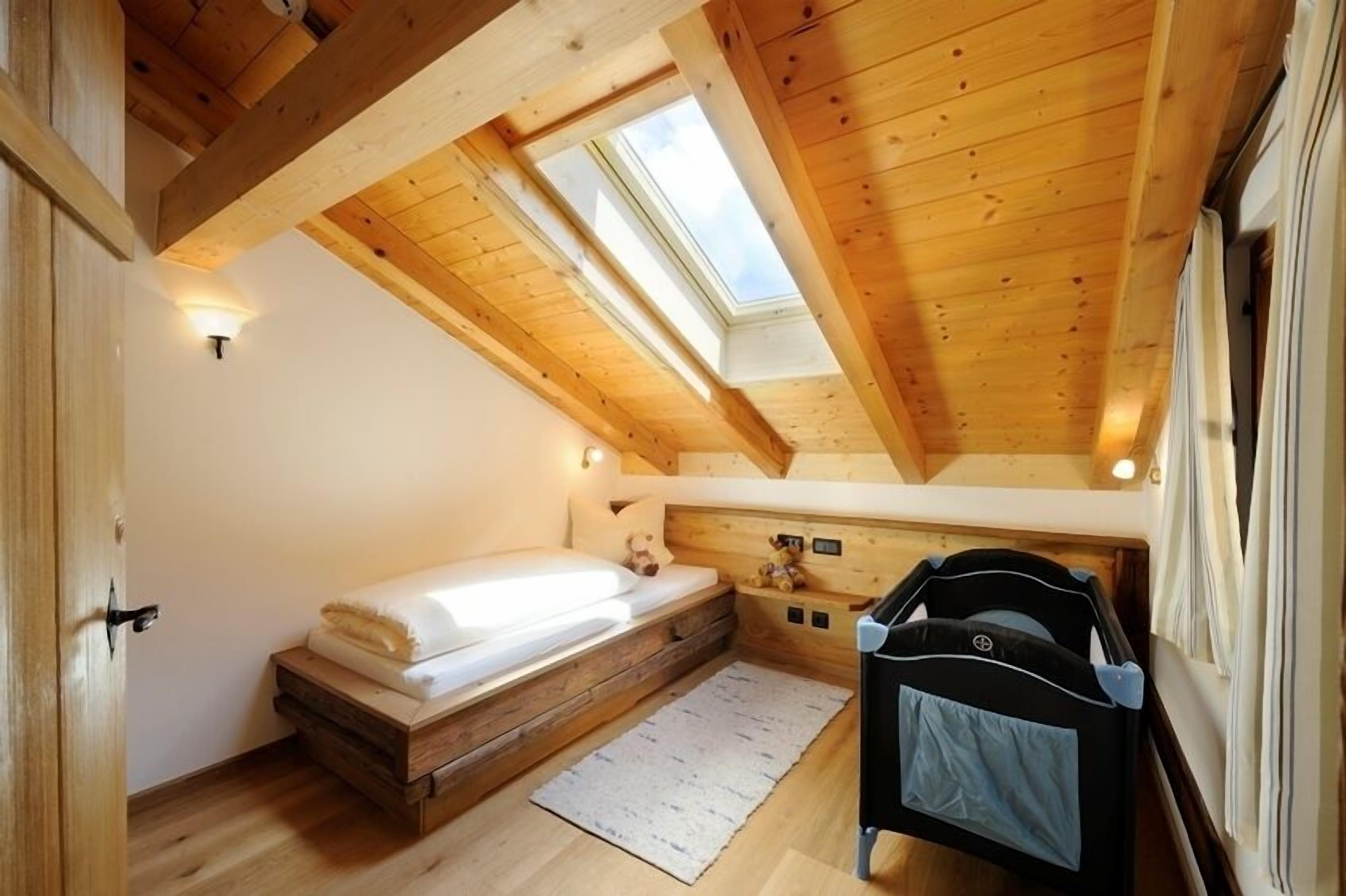 A small, cozy room with a sloped ceiling, skylights, a bed, a crib, and a small rug.