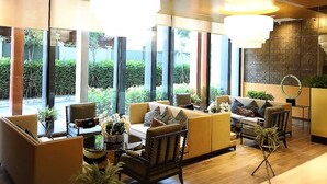 A modern lounge area with sofas, chairs, and a coffee table, featuring large windows and a staircase. - Astra Suites Central (Chiang Mai)