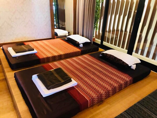 Two massage therapy beds with wooden floors and a window with curtains.