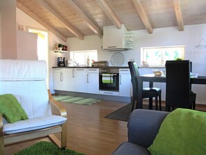 Una cocina moderna con armarios blancos, un comedor con mesa y sillas, y una sala de estar con sofá y cojines verdes.