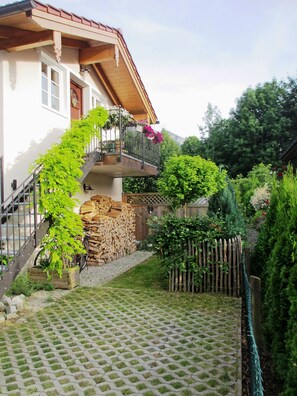 Una casa con balcón de madera, una escalera de piedra y un jardín con valla de madera.