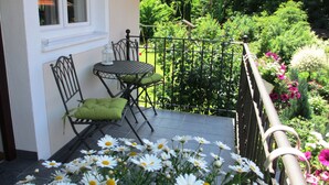 Ein Balkon mit Tisch und Stühlen, umgeben von üppigem Grün und Blumen.