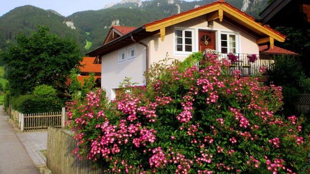 Ein Haus mit Balkon, umgeben von üppiger Vegetation und Bergen im Hintergrund.