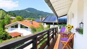 Uma varanda com vista para uma montanha, uma mesa com cadeiras e um vaso com girassóis.