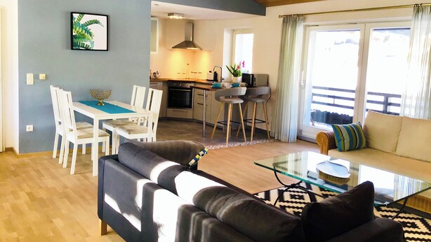 Uma sala de estar moderna com um sofá, uma mesa de centro de vidro e uma área de jantar com cadeiras e uma mesa.