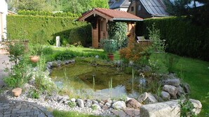 A serene garden with a pond, surrounded by a stone border and lush greenery. - Ferienwohnung für 3 Personen (Berchtesgaden)