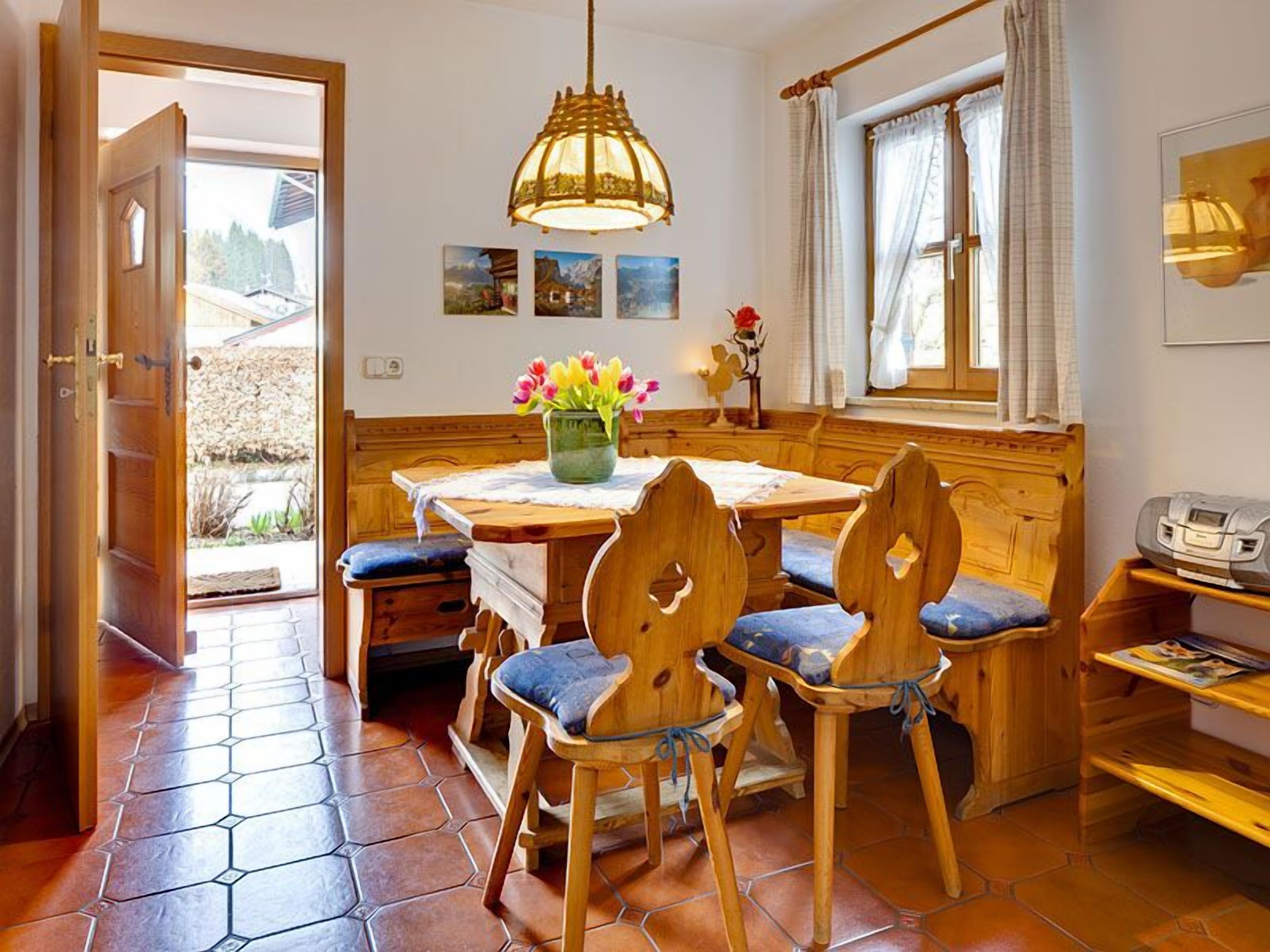 Ein gemütlicher Essbereich mit Holzmöbeln, einem Tisch mit Blumenvase und einem Fenster mit Vorhängen.