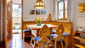 A cozy dining area with wooden furniture, a table with a vase of flowers, and a window with curtains. - Ferienwohnung für 3 Personen (Berchtesgaden)