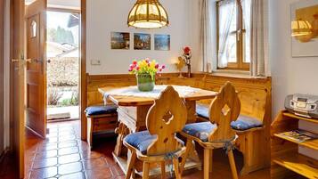 Ein gemütlicher Essbereich mit Holzmöbeln, einem Tisch mit Blumenvase und einem Fenster mit Vorhängen.