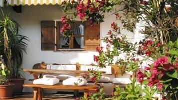 Eine Terrasse mit Holztisch und -stühlen, umgeben von Kübelpflanzen und blühenden Weinreben.