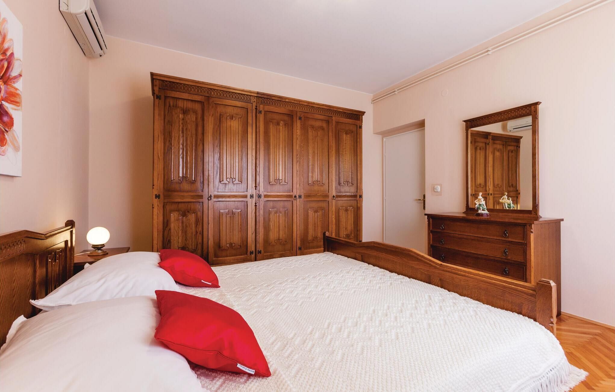 A bedroom with a large wooden wardrobe, a bedside table with a lamp, and a dresser with a mirror.