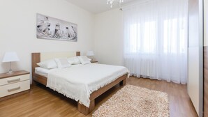 Un dormitorio con cama, mesitas de noche, candelabro, un cuadro y cortinas traslúcidas.