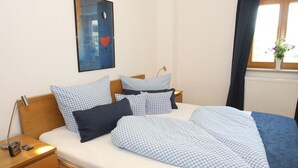 Una cama bien hecha con ropa de cama a cuadros, una mesita de noche con una lámpara y una obra de arte en la pared.