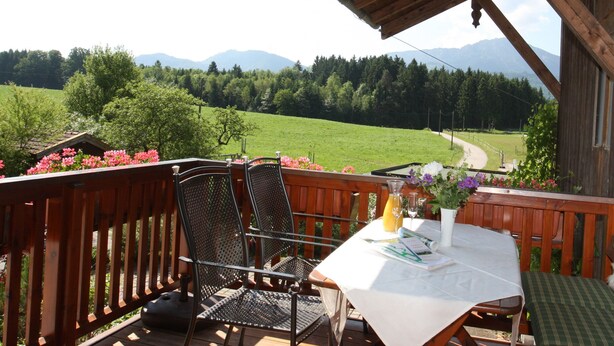Una terraza de madera con una mesa, sillas y vistas a un valle verde y montañas.